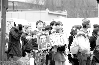 图为3月11日下午东京市内反对核电站的游行队伍。一名年轻男子手持批评野田首相是骗子的图片。他身旁的女性手中的牌子上写着“核电站的废弃物将残留10万年”。严圣禾摄 图为3月11日下午东京市内反对核电站的游行队伍。一名年轻男子手持批评野田首相是骗子的图片。他身旁的女性手中的牌子上写着“核电站的废弃物将残留10万年”。严圣禾摄
