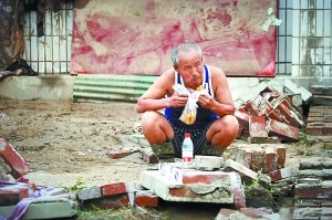 一位大叔在自家被冲毁的院子里吃晚饭,这是在暴雨之前剩下的一些烙饼。当前村民面临食物和饮水短缺。 一位大叔在自家被冲毁的院子里吃晚饭,这是在暴雨之前剩下的一些烙饼。当前村民面临食物和饮水短缺。