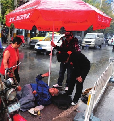 小伙儿一边为老人撑伞,一边询问他的伤情。 小伙儿一边为老人撑伞,一边询问他的伤情。