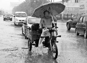 昨天,在王四营桥附近,一位骑三轮车的大爷打着伞在雨中前行。晨报记者 王巍/摄