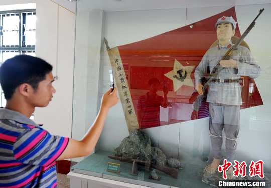 红色小上海陈列馆里,一名青年用手机拍下中国工农红军第四军军服留念